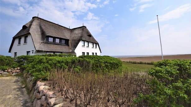 A white house with a thatched roof, surrounded by greenery and a clear sky. - House Stedum Apartment 19 (Sylt)