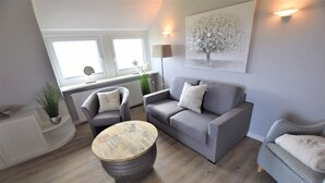 A modern living room with a grey sofa, two armchairs, a coffee table with a vintage design, and a painting on the wall. - House Stedum Apartment 19 (Sylt)