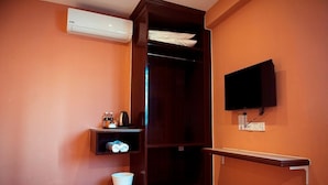 A hotel room with a wooden wardrobe, a small shelf with toiletries, a white bucket, and a mounted TV. - Q Collection @ Macalister(formerly know as Apple Hotel Penang)  (George Town)