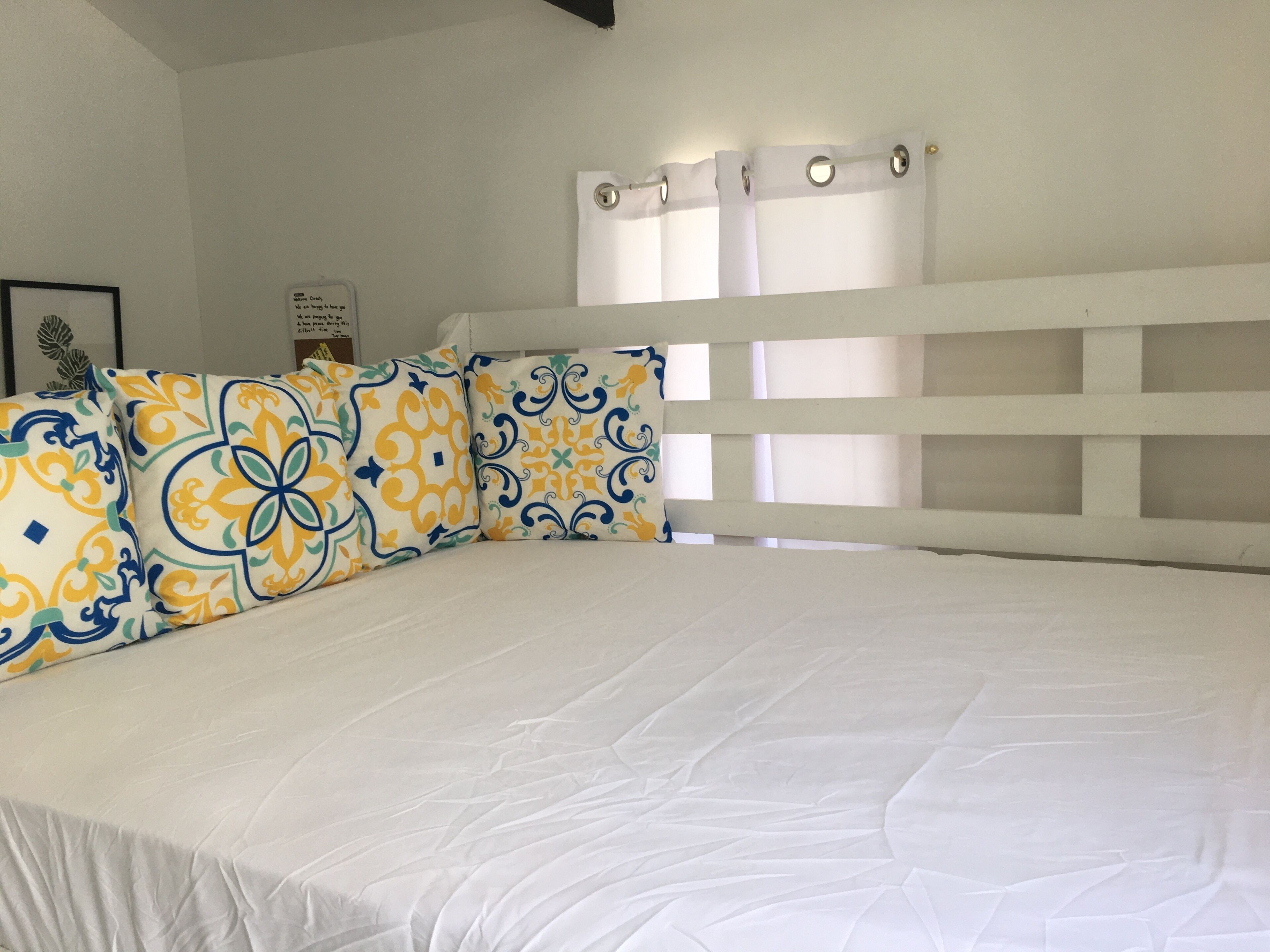 A bed with white bedding and decorative pillows, a white headboard, and a window with curtains.