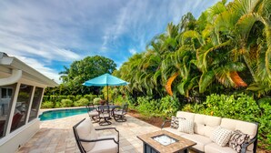 A patio with a pool, outdoor furniture, and lush greenery.