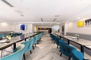 A modern dining area with long tables and teal chairs, a kitchen in the background, and a city view. - Hangzhou JinHang Hotel (Zhongfa Aviation Institute of Beihang University) (Hangzhou)