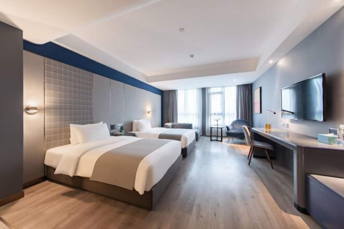 Ein Hotelzimmer mit zwei Betten, einem Schreibtisch, einem Fernseher und Blick auf die Stadt.
