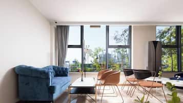 Una sala de estar moderna con un sofá azul, una mesa de comedor con sillas y grandes ventanales con vistas a la ciudad.