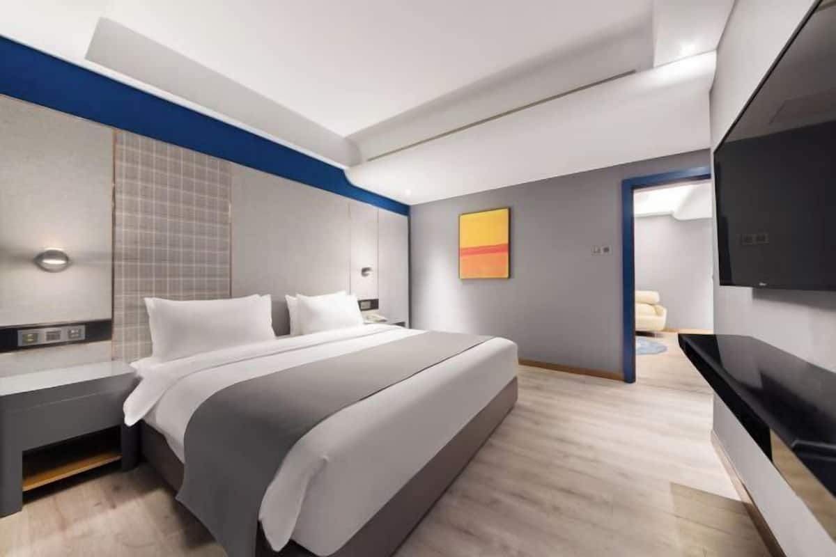 Ein modernes Hotelzimmer mit einem großen Bett, einem Flachbildfernseher, einem Nachttisch und einer wandmontierten Leuchte.