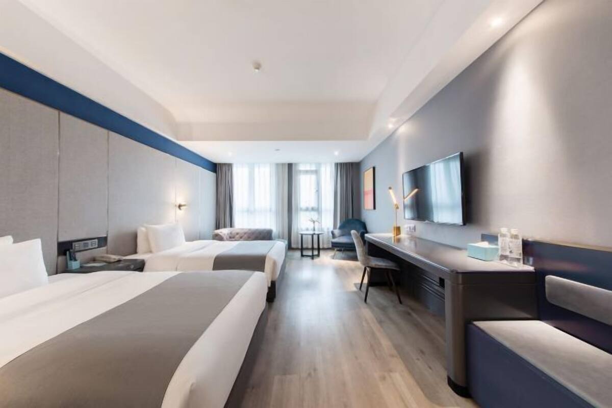 Ein Hotelzimmer mit zwei Betten, einem Schreibtisch, einem Stuhl, einem Fernseher und einem Fenster mit Vorhängen.