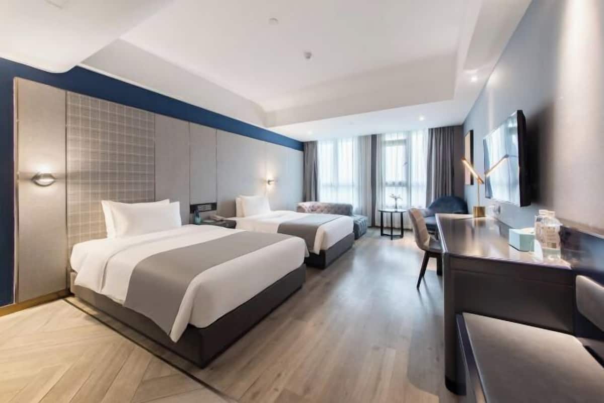 Ein Hotelzimmer mit zwei Betten, einem Schreibtisch, einem Stuhl, einem Fernseher und einem Fenster mit Vorhängen.