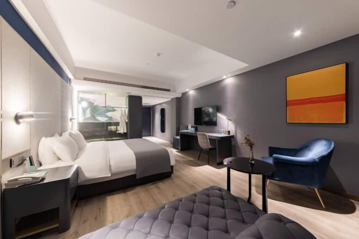 Ein modernes Hotelzimmer mit Bett, Schreibtisch, Sessel und Fernseher.