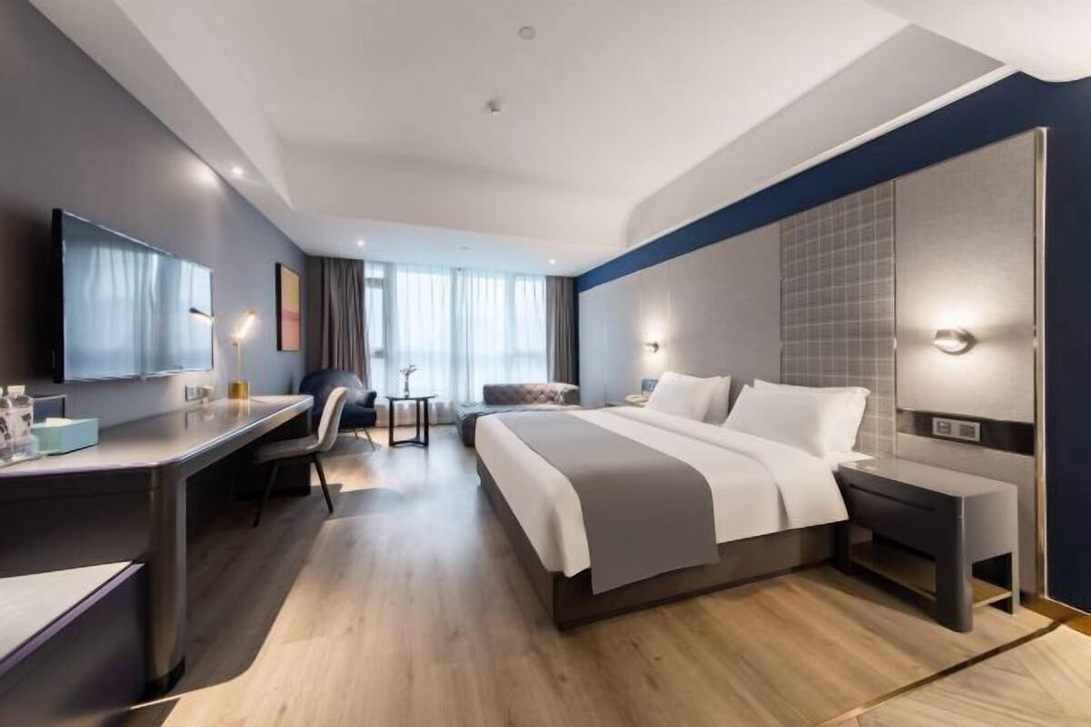 Ein modernes Hotelzimmer mit einem großen Bett, einem Schreibtisch, einem Stuhl und einem Fernseher.