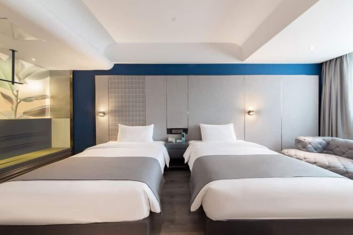 Ein Hotelzimmer mit zwei Betten, einem großen Spiegel, einem Nachttisch und einer gepolsterten Sitzecke.