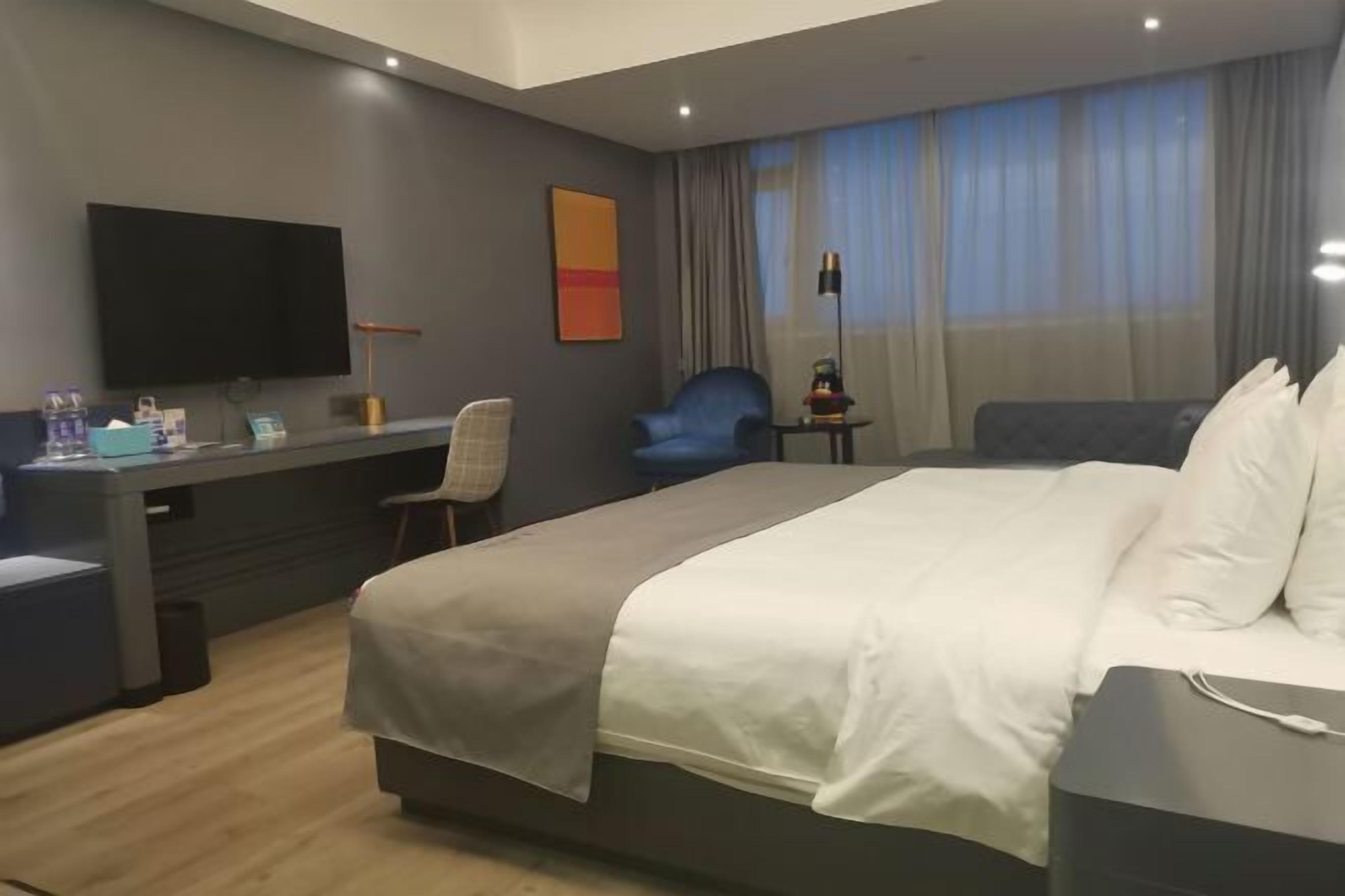 Habitación de hotel con cama, escritorio, silla, televisión y ventana con cortinas.