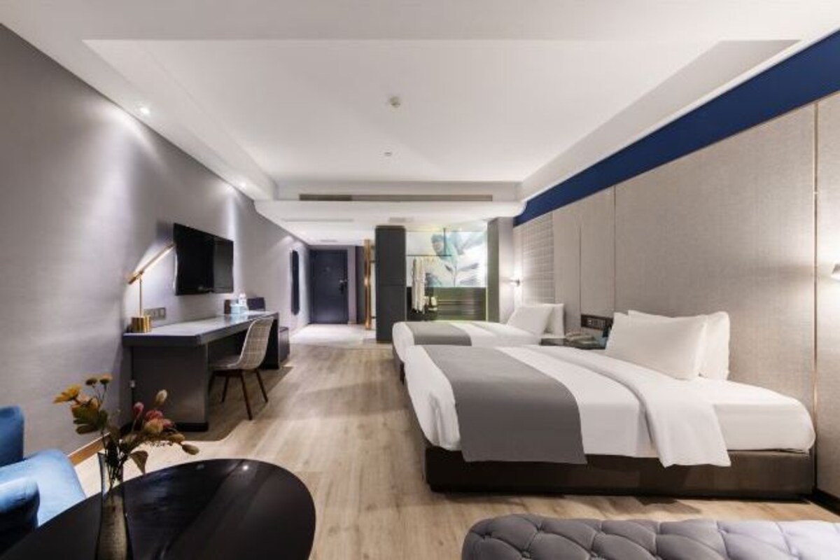A modern hotel room with a large bed, a desk, a chair, and a TV.