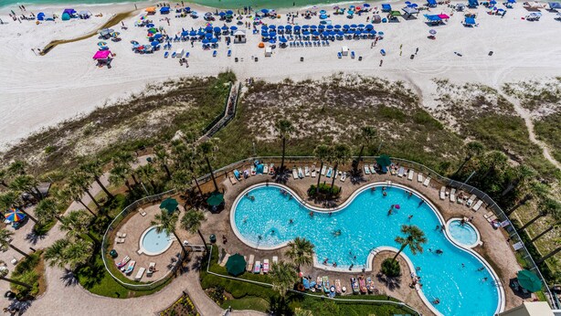 An aerial view of a resort with a large pool, beach area with umbrellas, and palm trees. - PET FRIENDLY! GREAT VIEWS! UPDATED FURNISHINGS! BCH SRVC INCL!!! (Panama City Beach)