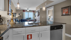 A modern kitchen with granite countertops, white cabinetry, and a built-in dishwasher. - PET FRIENDLY! GREAT VIEWS! UPDATED FURNISHINGS! BCH SRVC INCL!!! (Panama City Beach)
