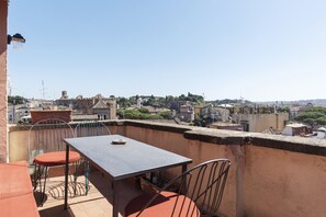 A rooftop terrace with a table and chairs, overlooking a cityscape with historical buildings.