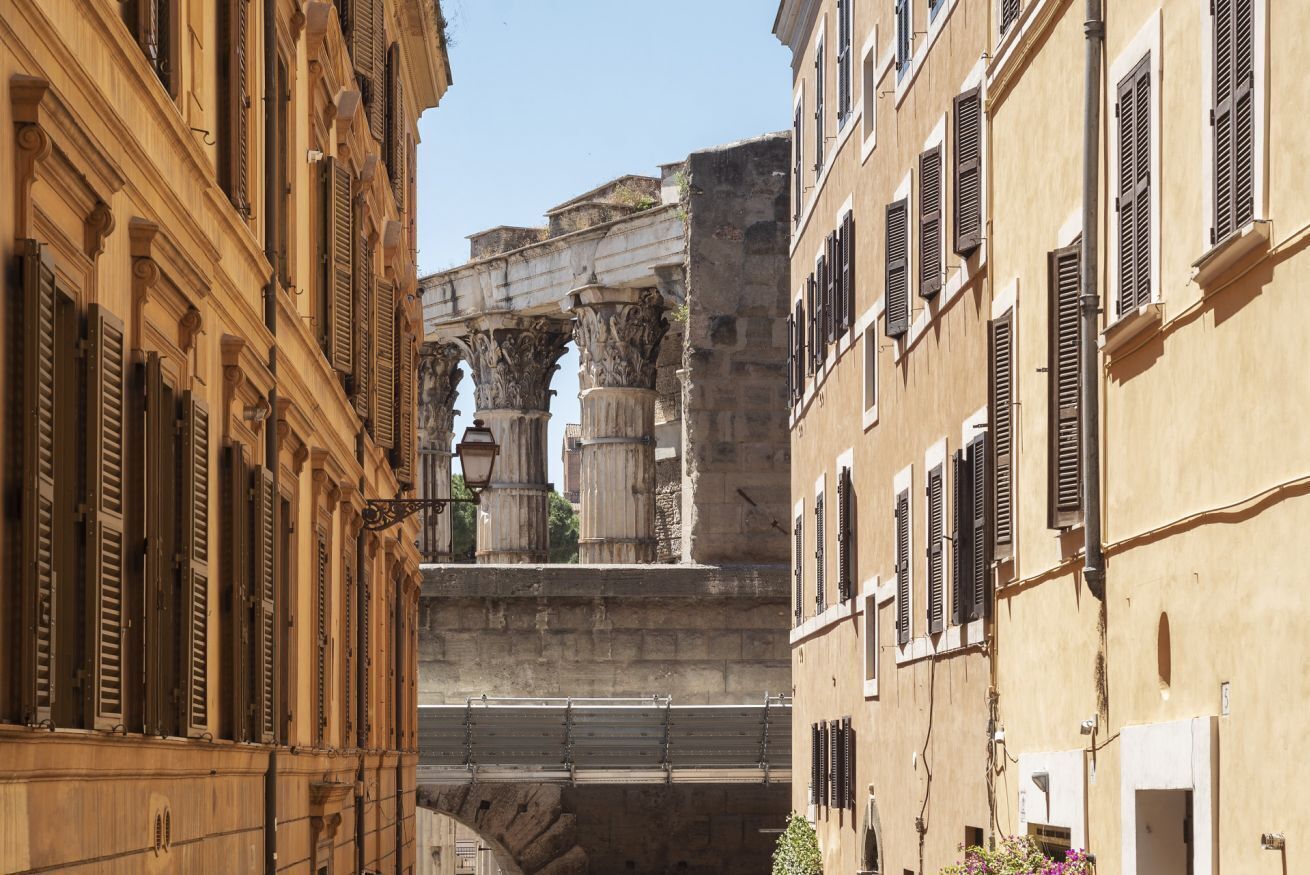A narrow street with historic stone buildings, a stone bridge, and a classical archway.