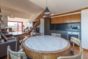 A modern living room with a marble coffee table, wooden chairs, and a staircase leading to a kitchen with wooden cabinets and a built-in oven. - Spectacular attic with private terrace in central Rome - Wifi, Heating, A/C (Roma)