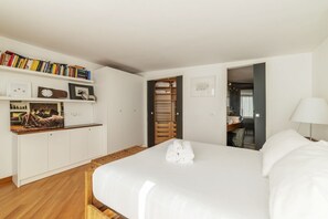 A hotel room with a large bed, a wardrobe, a bedside table with a lamp, and a bookshelf with books and framed pictures. - Spectacular attic with private terrace in central Rome - Wifi, Heating, A/C (Roma)