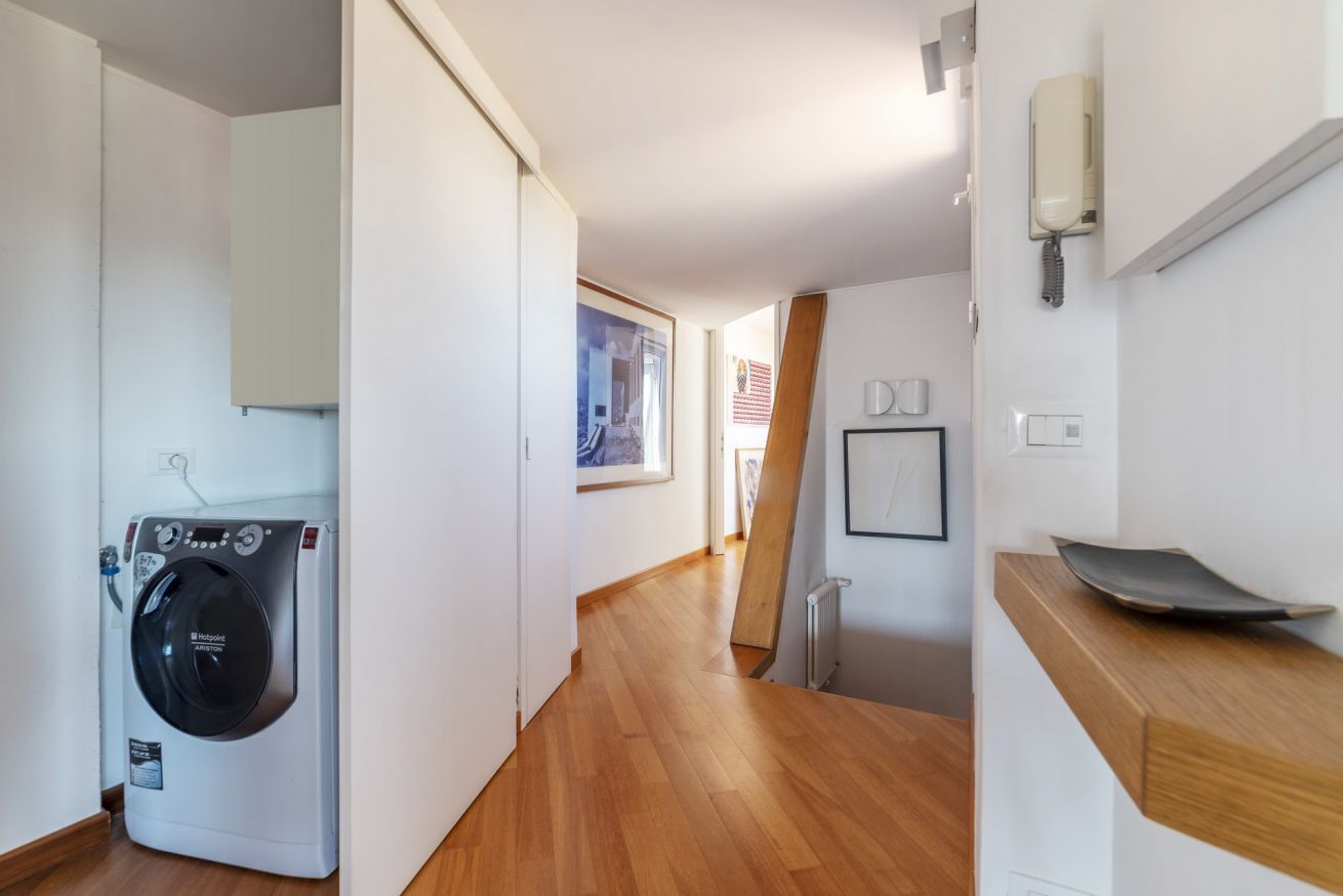 Un cuarto de lavandería con lavadora de carga frontal, piso de madera y un pequeño mostrador de madera.