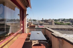 A rooftop terrace with a table and chairs, overlooking a cityscape with historical buildings and a clear sky.