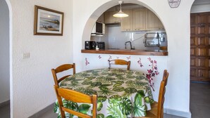 A dining area with a table covered in a tropical leaf tablecloth, wooden chairs, and a framed picture on the wall. - Pleasant sea view apartment (Empuriabrava)