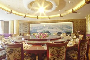 Una mesa de comedor redonda con centros de mesa florales, rodeada de sillas ornamentadas, en una habitación con un mural grande y papel tapiz estampado.