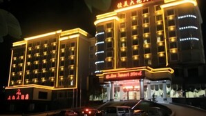 Et hotel med flere etager, oplyst skiltning og parkeringsplads.