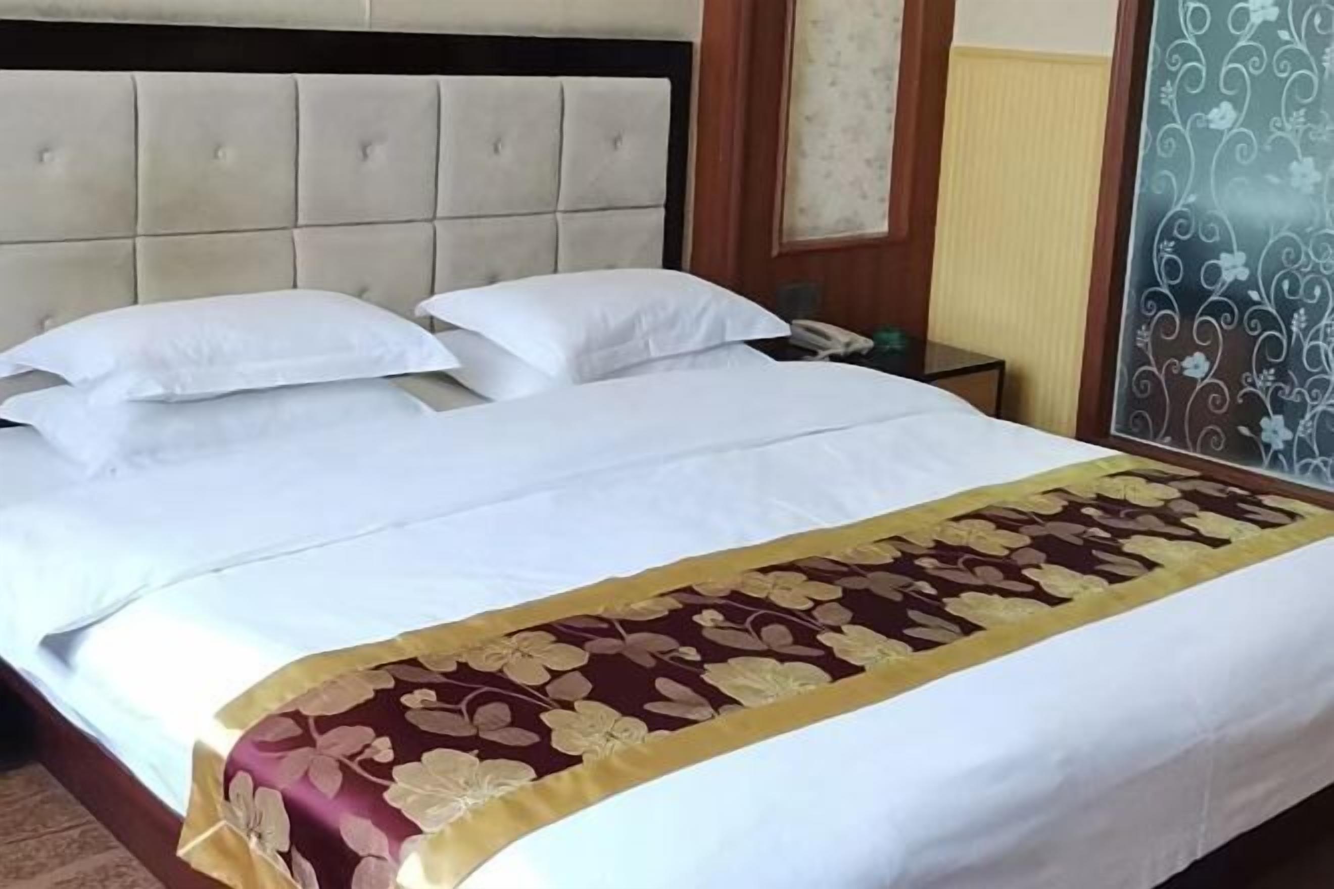 Una cama con sábanas blancas, una colcha de estampado floral y un cabecero acolchado.