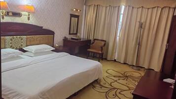 Habitación de hotel con una cama grande, un escritorio, una silla, un espejo y una ventana con cortinas.
