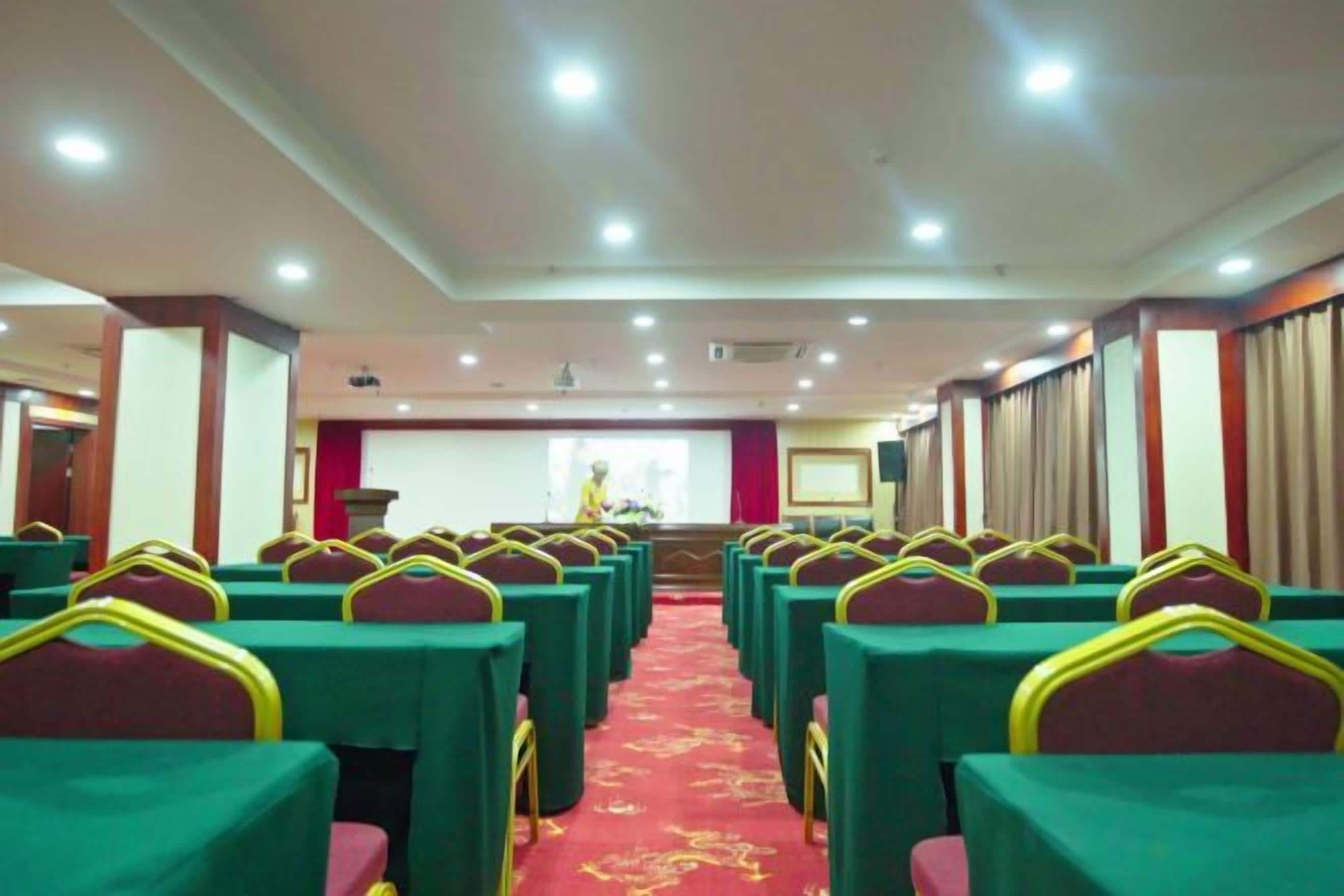 A conference room with rows of tables and chairs, a podium, and a presentation screen.