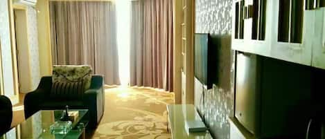 A hotel room with a sofa, a glass coffee table, a flat-screen TV, and a patterned carpet.