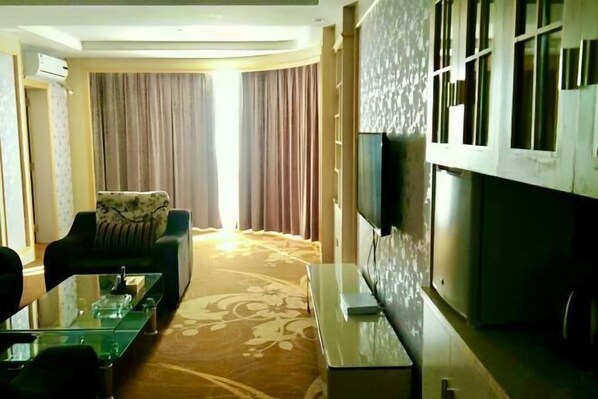 A hotel room with a sofa, a glass coffee table, a flat-screen TV, and a patterned carpet. - Junmei International Hotel (Jiangbin Cultural Square Branch) (Dahua)
