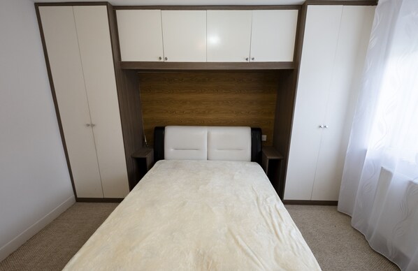 A bedroom with a bed, a wooden headboard, two nightstands, and a wardrobe with two doors.