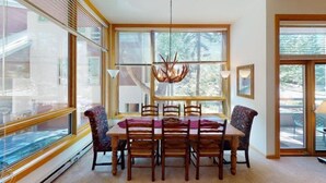 A dining area with a table and chairs, large windows, and a ceiling light fixture. - Westhaven 3 Bedroom Luxury Condo in Cascade Village, Steps to Chair Lift (Vail)