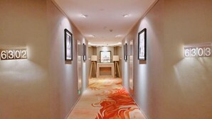 A hotel hallway with numbered doors, framed artwork on the walls, and a carpet with a red and orange pattern. - Bingly Hotel (White Feather Road, Xixia, Nanyang) (Xixia)