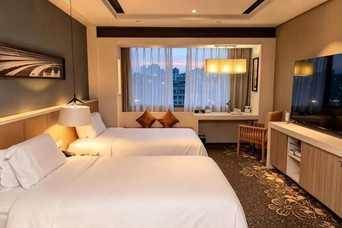Een hotelkamer met twee bedden, een bureau, een televisie en een raam met uitzicht over de stad.