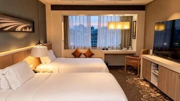 Habitación de hotel con dos camas, un escritorio, televisión y ventana con vista a la ciudad.