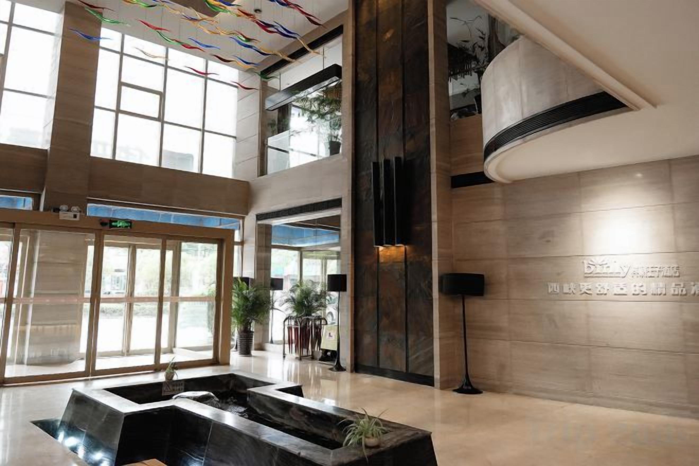 A hotel lobby with a large reception desk, a water feature, and a high ceiling with natural light.