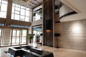 Vestíbulo de hotel con una amplia recepción, un elemento decorativo de agua y un techo alto con luz natural.