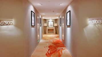 A hotel hallway with numbered doors, framed artwork, and a carpet with a swirling pattern.