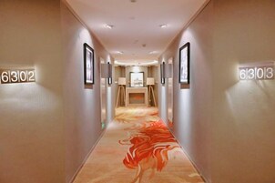 Un pasillo de hotel con puertas numeradas, cuadros enmarcados y una alfombra de diseño espiral.