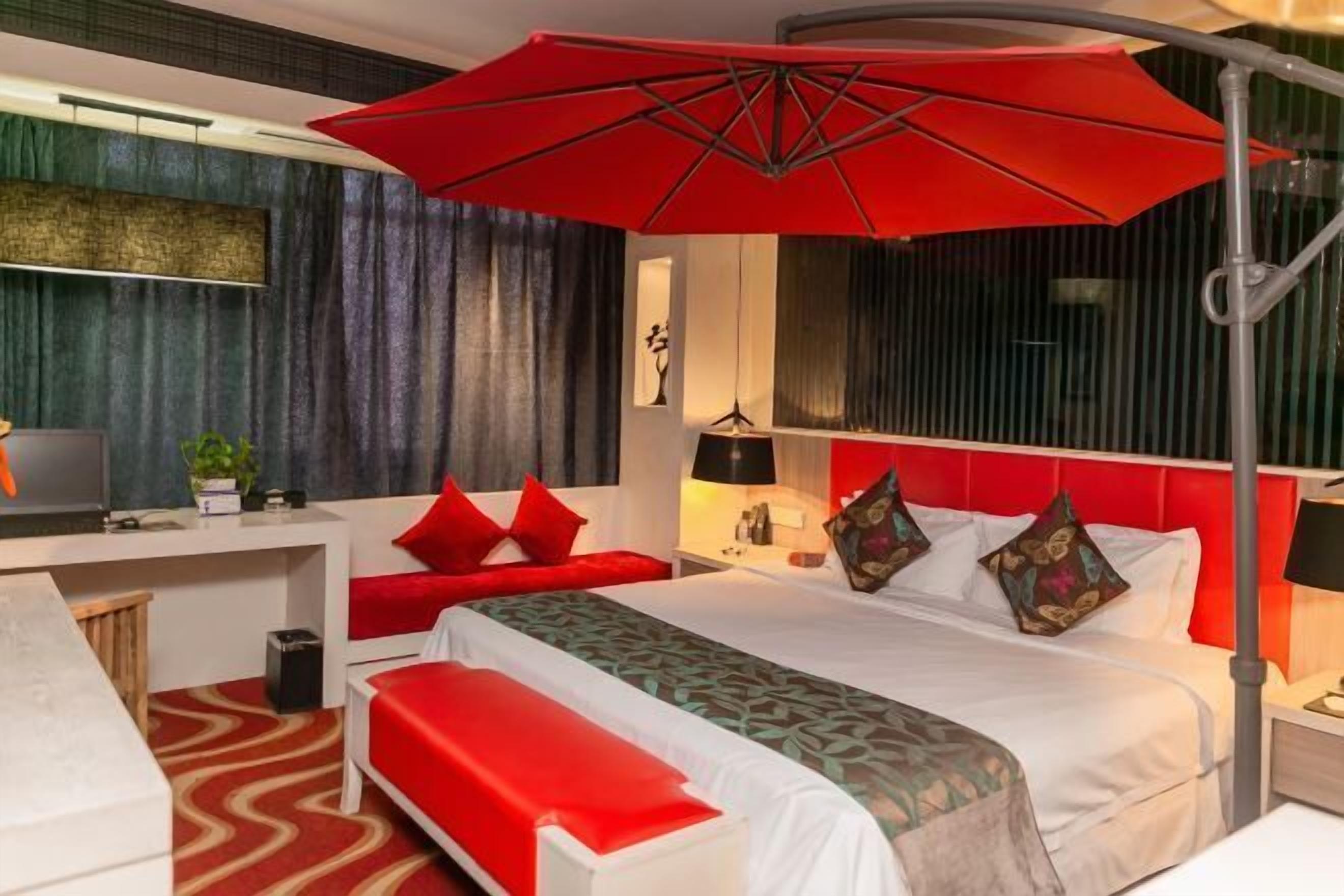 Ein Hotelzimmer mit Bett, Schreibtisch, Sitzbank, einem roten Regenschirm und einem Fernseher.