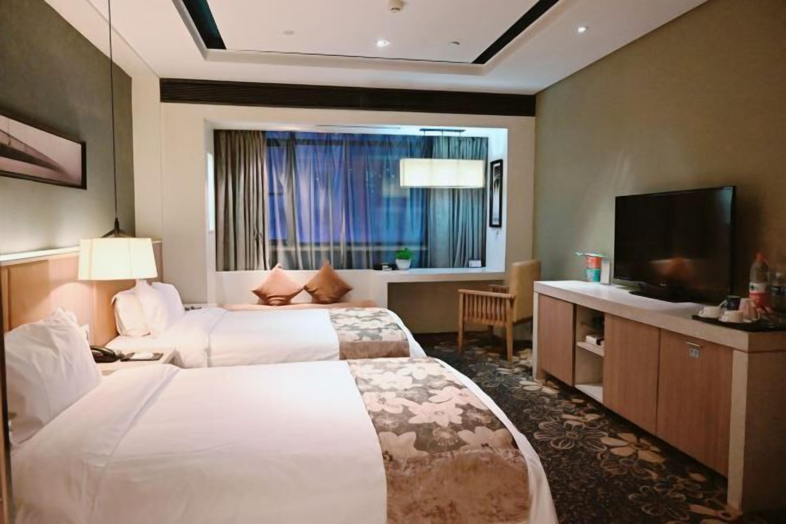 Ein Hotelzimmer mit zwei Betten, einem Fernseher, einem Schreibtisch und einem Fenster mit Vorhängen.