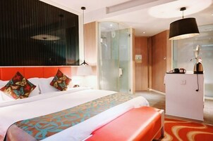 Habitación de hotel con cama, escritorio, cabina de ducha de vidrio y un banco rojo.