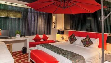 A hotel room with a bed, a desk, a red umbrella, and a red bench.
