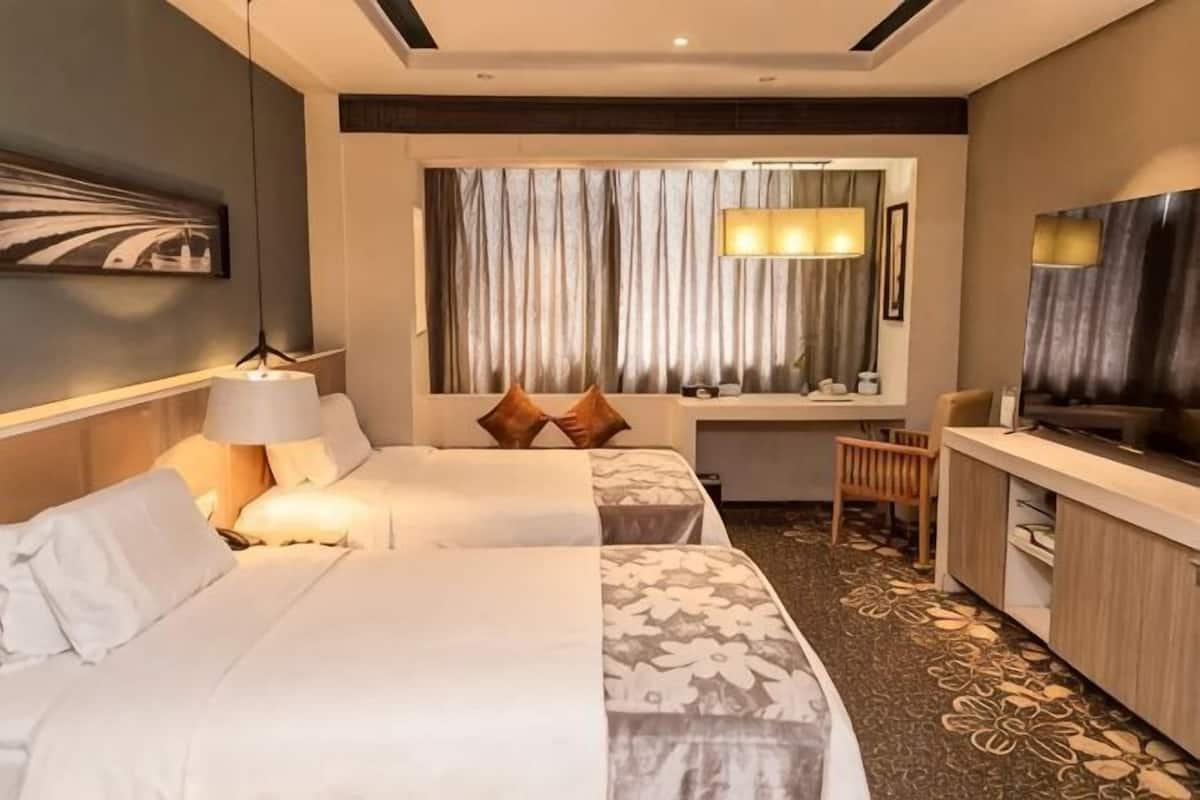 Een hotelkamer met twee bedden, een bureau, een televisie en een raam met gordijnen.