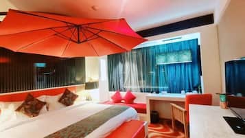 A hotel room with a large bed, a desk, a chair, a window with curtains, and a red umbrella.