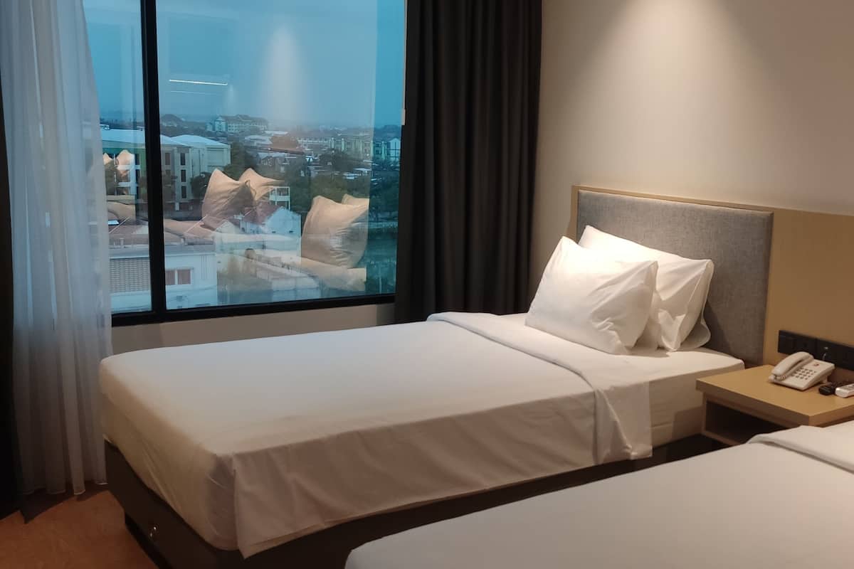 A hotel room with two beds, a nightstand with a phone, and a view of the city through large windows.