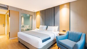 A modern hotel room with a large bed, a blue armchair, and a glass partition wall. - EASTERN HOTEL BOJONEGORO (Bojonegoro)