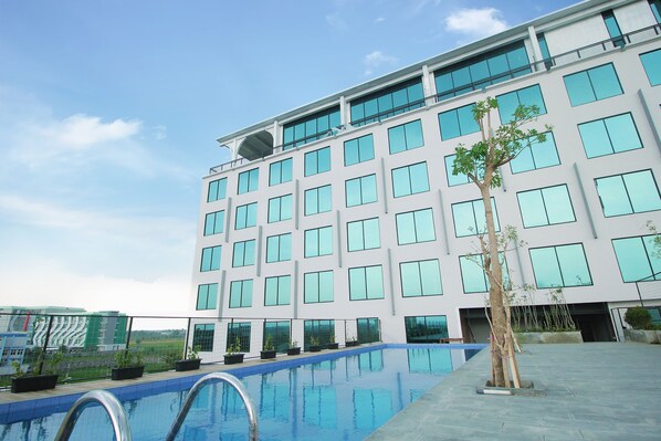 A modern hotel with a swimming pool, large windows, and a flat roof.